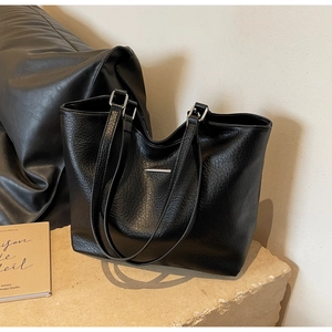 Detail of black pebbled leather tote bag with silver metal bar on stone pedestal