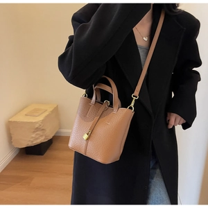 Close-up of caramel bucket bag with lychee texture and gold lock detail on black blazer