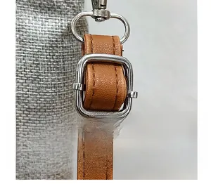 Detail of adjustable brown leather shoulder strap with silver metal buckle on linen bag