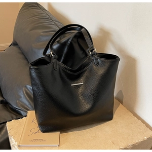 Detail of black pebbled leather tote bag with silver trim on a stone pedestal