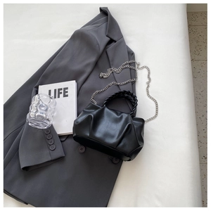 Detail of black pleated crossbody bag with woven handle and silver chain on a suit jacket