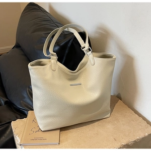 Close-up of beige tote bag with pebbled leather texture and silver metal bar detail
