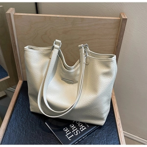 Macro detail of creamy white lychee grain tote bag showing metal logo and soft texture