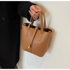 Detail of brown pebble leather bucket bag featuring a gold padlock and dual handles