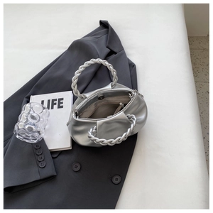 Detail of silver pleated cloud bag featuring woven handle and magnetic snap closure