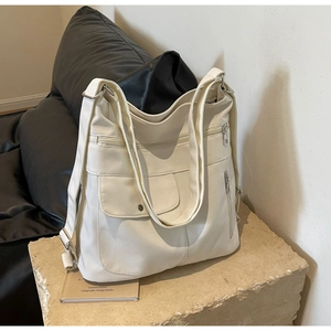 Detail view of cream leather shoulder bag featuring multi-pocket design and metal zippers
