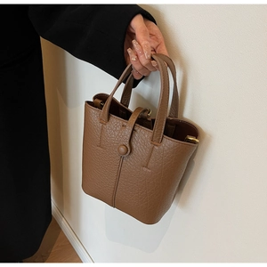 Close-up of brown lychee grain leather bucket bag with top handle and button closure