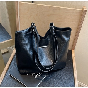 Detail of black pebbled leather tote bag featuring silver hardware on a minimalist background