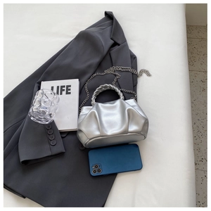 Detail of silver pleated cloud bag with metallic woven handle and chain on a suit jacket