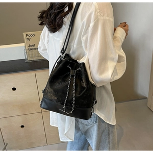 Detail of black drawstring bucket bag with wavy texture and silver chain strap for women