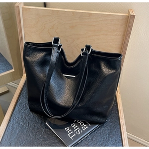 Detail of black lychee grain leather tote bag with silver hardware on a wooden chair