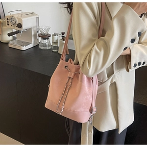 Detailed close-up of a pink suede bucket bag with metal chain drawstring and leather strap