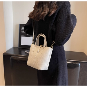 Detail view of the cream lychee grain leather bucket bag worn by a model in black dress