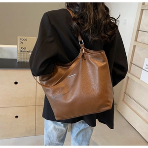 Detailed close-up of brown litchi grain leather tote bag with silver metal bar decoration