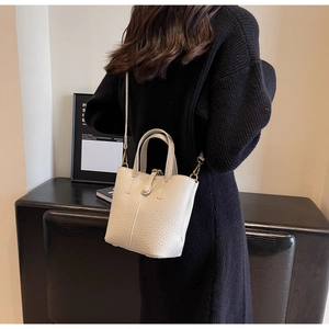 Detail of minimalist cream bucket bag with lychee grain texture and gold hardware details