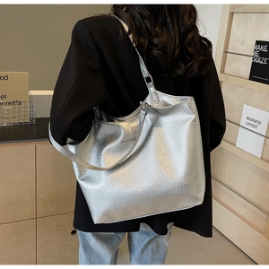 Detail of silver metallic tote bag with lychee texture carried by a model in a modern office