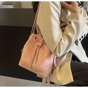 Detail of pink suede bucket bag featuring a decorative metal chain and drawstring closure