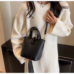 Close-up of black bucket bag with lychee grain texture and gold hardware on white sweater
