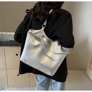Detail view of a large silver metallic tote bag featuring pleated texture and wide shoulder strap