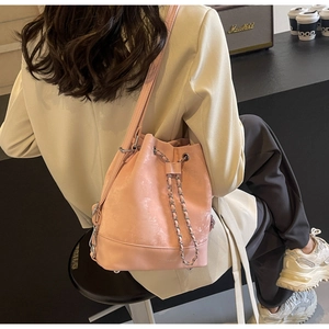 Pink bucket bag with drawstring and chain detail worn by model in casual urban setting