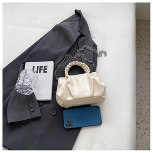 Detail view of cream pleated handbag with woven handle and silver chain on a suit jacket