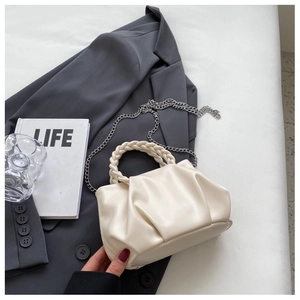 Detail of cream pleated crossbody bag with woven handle and silver chain on a desk