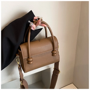 Détail du sac bandoulière en cuir marron avec une large sangle d'épaule tissée