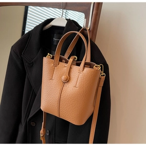 Close-up of brown litchi grain leather bucket bag with elegant round buckle and strap