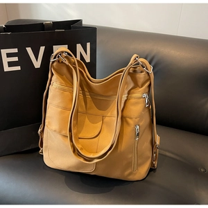 Detail of camel multifunctional shoulder bag with multiple zippers on black leather sofa