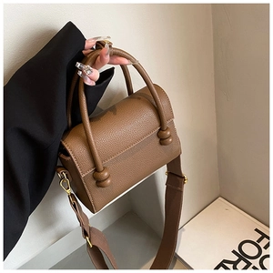 Détail du sac marron en cuir grainé avec une large bandoulière et fermoir doré