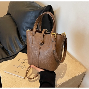 Close-up of caramel brown pebble leather bucket bag with gold hardware on stone surface