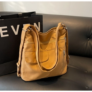 Detail of camel nylon shoulder bag with multiple silver zippers on a black sofa