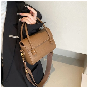Modèle portant un sac à main marron en cuir grainé avec bandoulière large et fermoir à perles