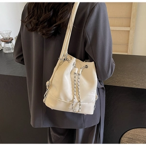 Detail of cream leather bucket bag with silver chain, drawstring, and metal protective feet
