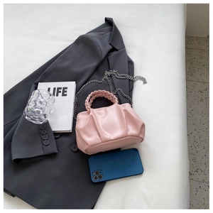 Pink pleated cloud bag detail featuring woven handle and silver chain on grey blazer