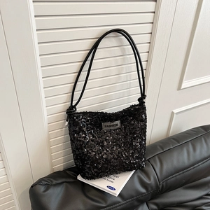 Trendy black sequin shoulder bag with leather straps and fashion label on leather sofa