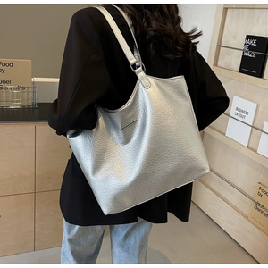 Detailed view of silver tote bag with lychee texture on black blazer shoulder