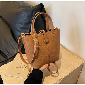 Close-up of brown litchi grain leather bucket bag with golden buckle and textured finish