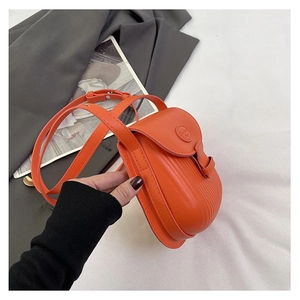 Detail shot of orange pleated crossbody bag featuring a circular logo on a blazer background