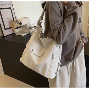 Detailed view of cream faux leather shoulder bag featuring a front pocket with metal clasp