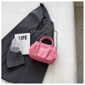 Detail view of pink pleated handbag with woven handle and metallic chain on a grey blazer