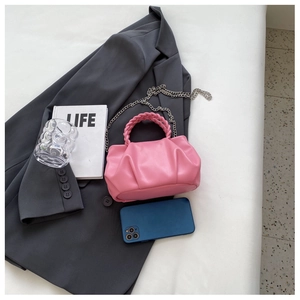 Pink pleated handbag with woven handle and silver chain strap on a blazer background