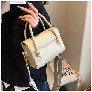 Détail du sac carré beige en cuir grainé avec une large bandoulière en tissu et boucles