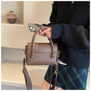 Détail du sac à main en cuir marron avec large bandoulière textile et ferrures dorées
