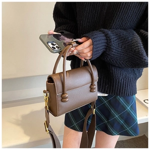 Détail du sac à main en cuir marron avec sphères dorées sur la poignée et bandoulière large