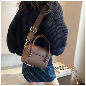 Sac bandoulière en cuir marron avec large sangle porté par un mannequin en tenue décontractée