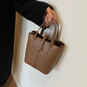 Minimalist dark brown bucket bag in lychee pattern leather held by a model in studio