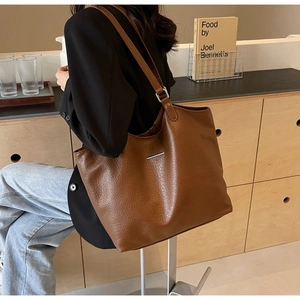 Detailed view of brown lychee-textured faux leather tote bag with silver metal accents