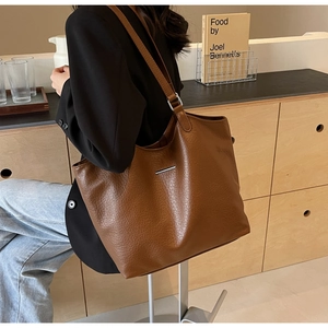Detail of a brown textured faux leather tote bag with a minimalist metal buckle decoration