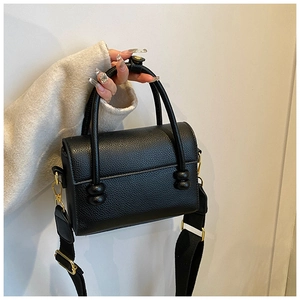 Détail du sac à main noir en cuir litchi avec ferrures dorées et large bandoulière tissée